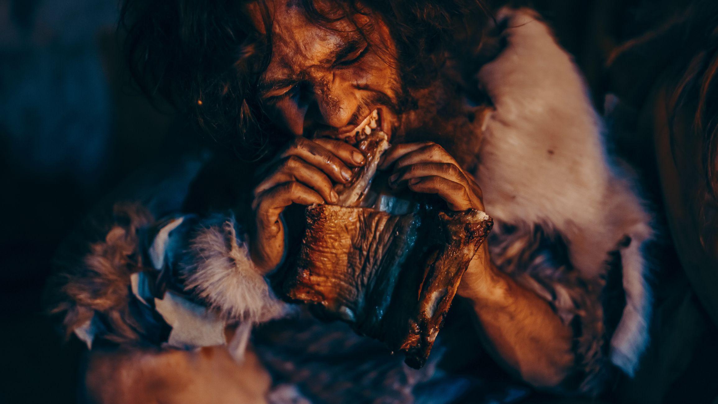 Retrato de cerca de un líder tribal vestido con piel de animal comiendo en una cueva oscura y tenebrosa por la noche. 