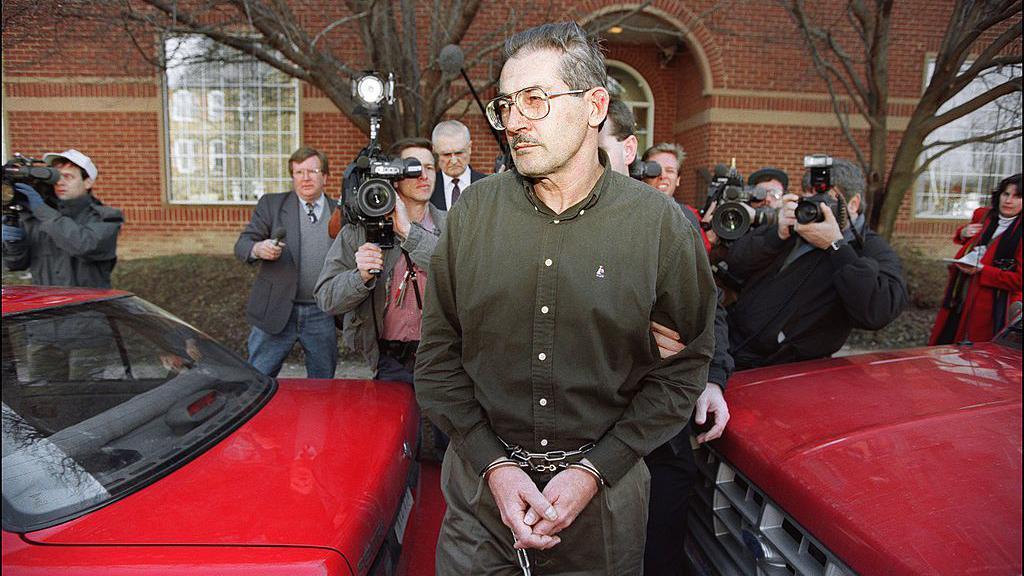 Aldrich Ames esposado y perseguido por varios periodistas y cámaras de televisión.