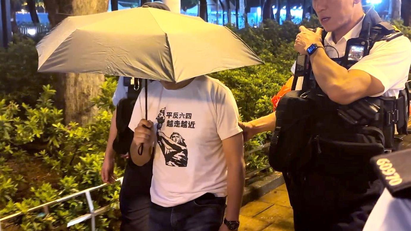 2025年6月4日，一名身穿「平反六四 越走越近」字樣及「民主女神」圖像上衣的男子在維園被警方帶上警車離開