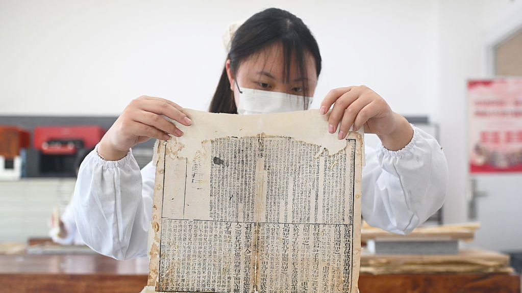 一個女生身著白褂，舉起一頁古籍文稿。