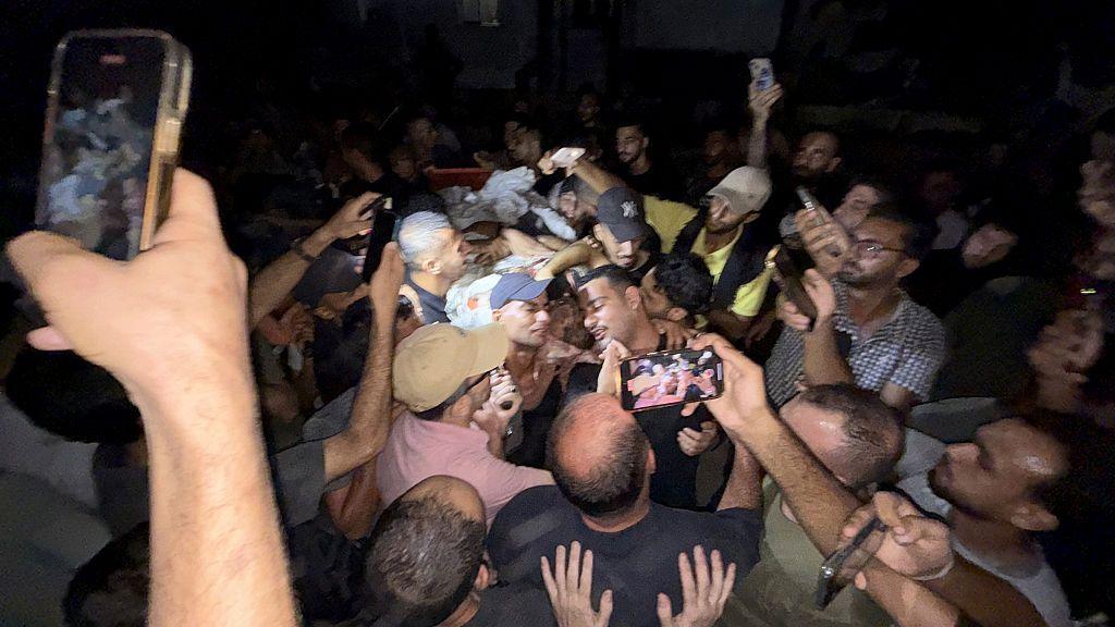 عدد من الأشخاص وكاميرات هواتف نقالة موجهة لجثمان الشريف الذي يحمله عدد من الفلسطينيين بعد استهدافه ليلاً.