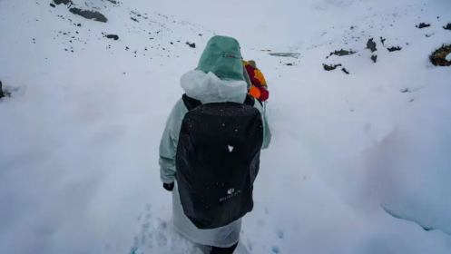 Un senderista vestido en ropa invernal, con una mochila en la espalda camina arduamente por un sendero lleno de nieve