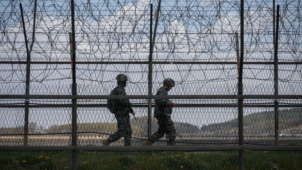 La cerca de alambre de púas con dos guardias que patrullan el área.