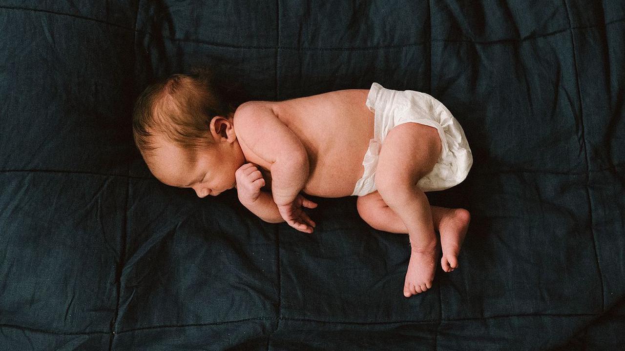 Un bebé a pocos días de nacido duerme en pañales sobre un fondo oscuro