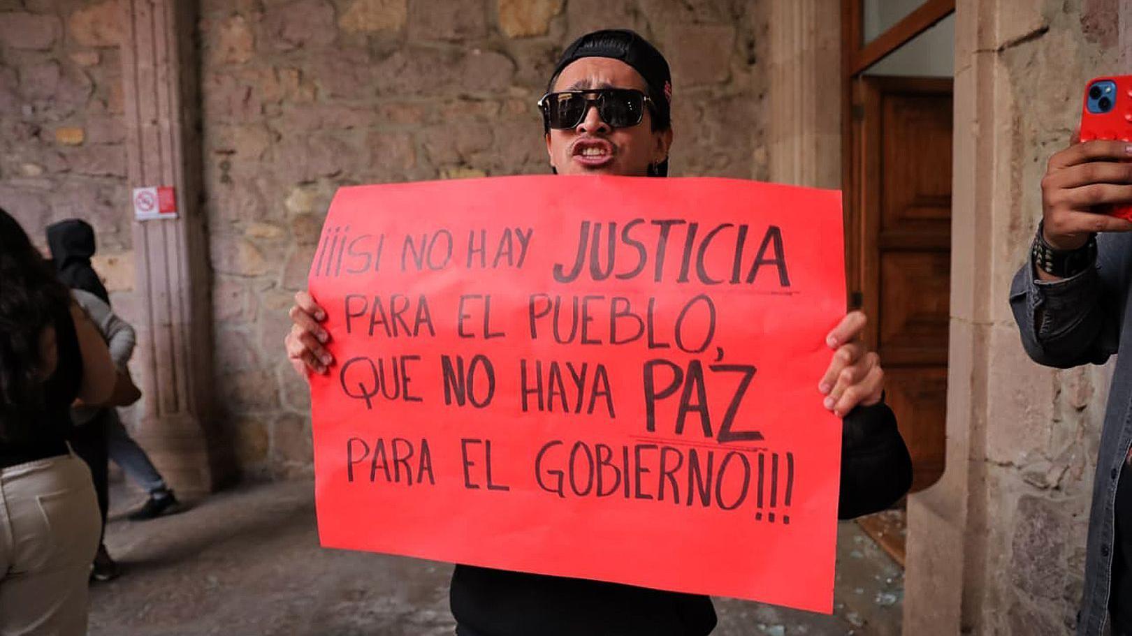 Un hombre sostiene un letrero rojo con un mensaje que reclama justicia en una manifestación.