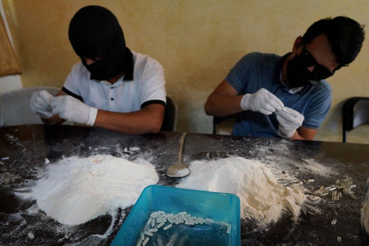 Personas haciendo pastillas de metanfetaminas con la cara cubierta.