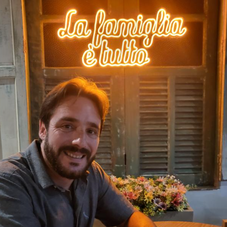 Dono de restaurente italiano sorri em frente de um painel luminoso que diz: La familgia &eacute; tutto