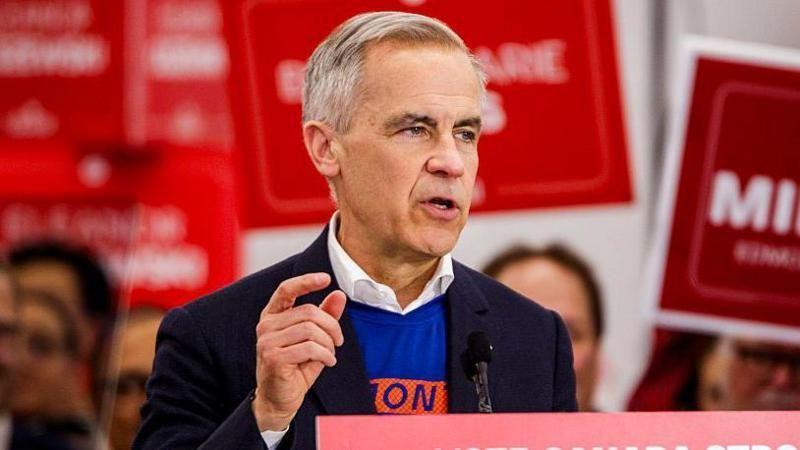 Primeiro-ministro canadense Mark Carney discursa em comício eleitoral, com bandeiras do seu partido ao fundo