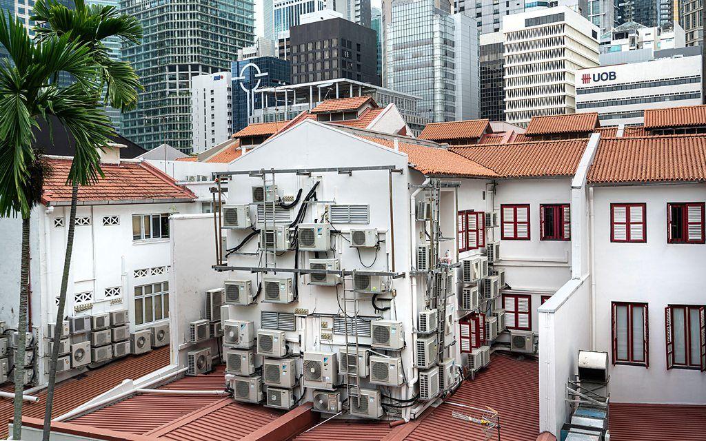 Un conjunto de edificaciones en Singapur con múltiples equipos de aire acondicionado sobre sus paredes exteriores.