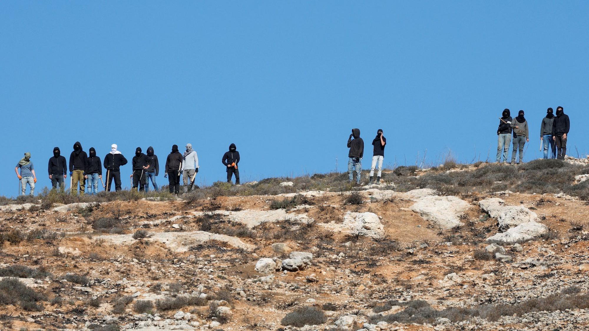 Israeli settlers with covered faces and hoods are carrying bats and sticks.