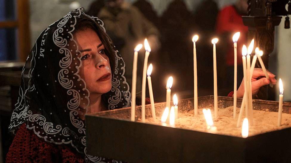 Mujer encendiendo una vela en la Iglesia Griega Ortodoxa de San Porfirio