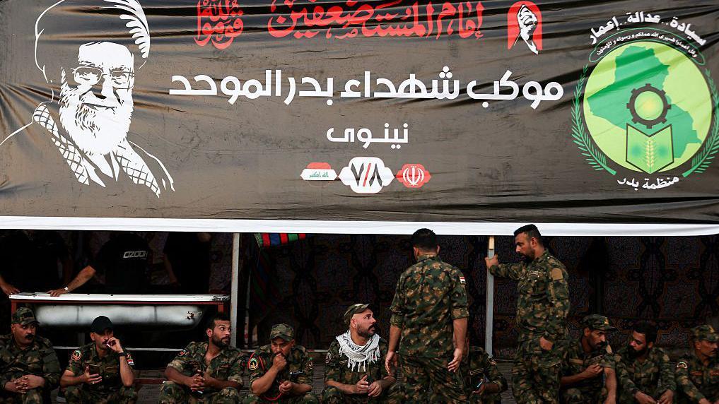 جنود عراقيون يجلسون تحت لافتة سوداء كبيرة عليها صورة خامنئي وعبارة إمام المستضعفين