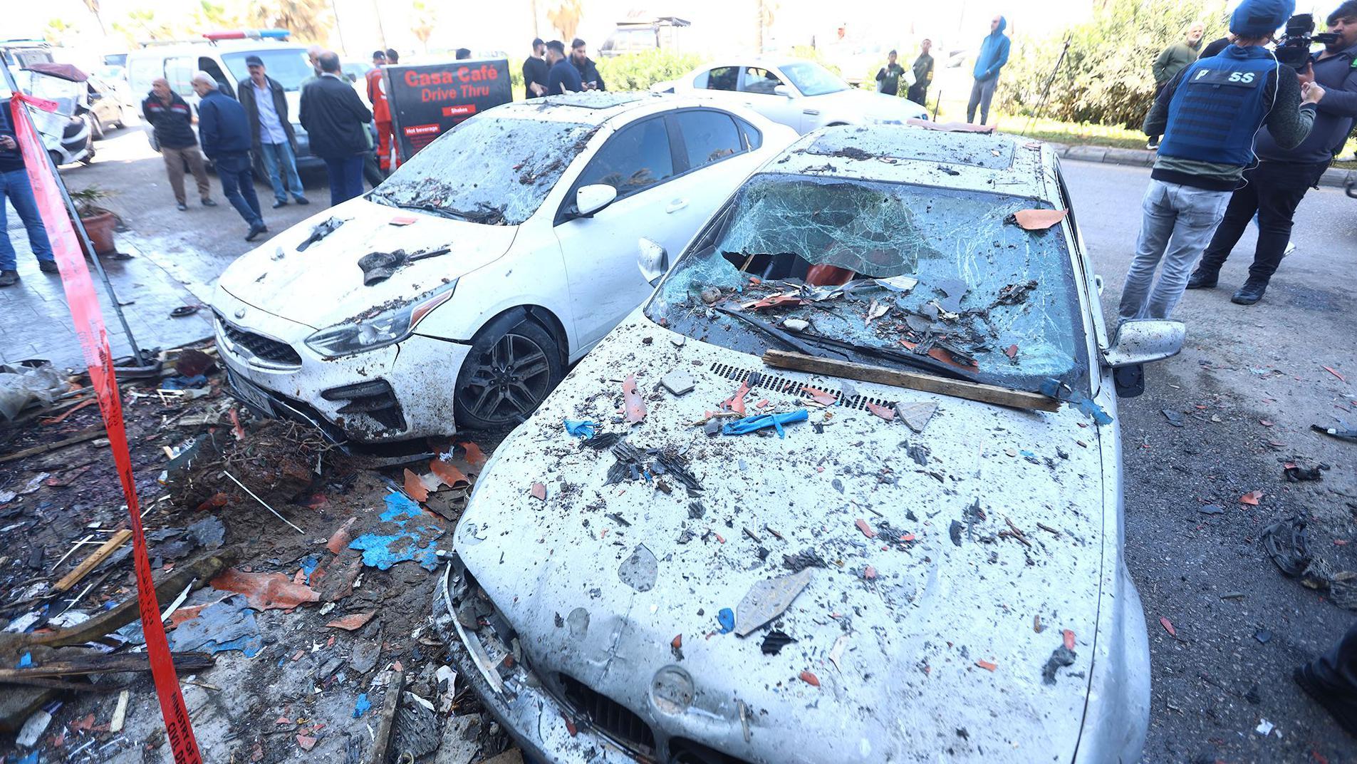 En la imagen aparecen dos automóviles dañados y cubiertos de escombros, con multitudes de personas en la calle de fondo y ruinas tras un ataque con misiles israelíes en la carretera costera de Sidón este miércoles.