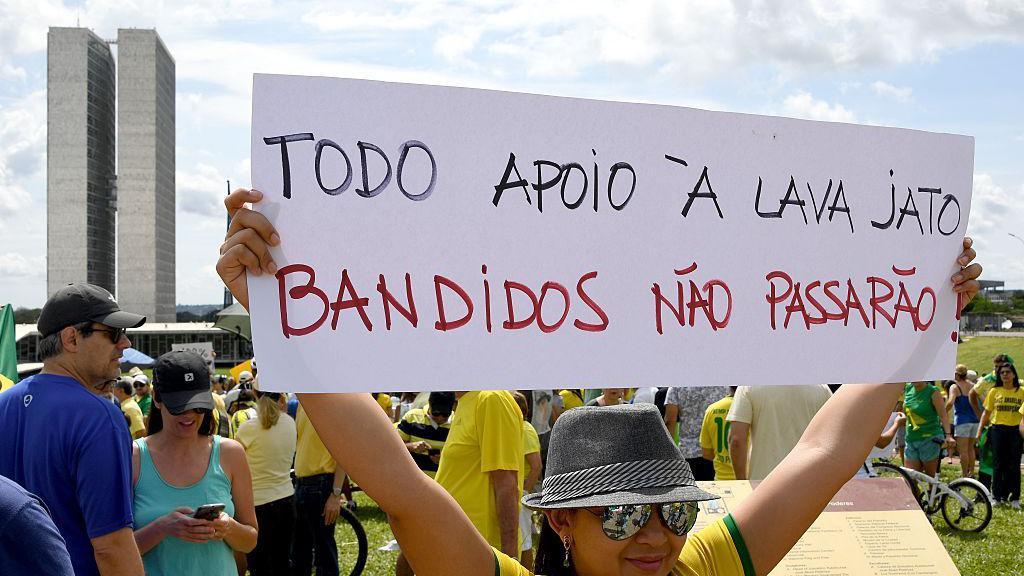 Uma mulher vestindo a camiseta da Sele&ccedil;&atilde;o brasileira segura um cartaz em que se l&ecirc; 