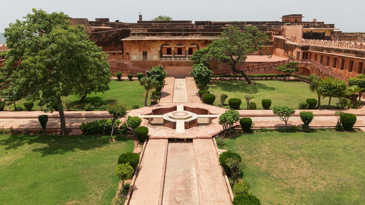 Espa&ccedil;o dividido em quatro jardins verdes, cruzados por quatro canais que chegam ao centro, onde h&aacute; uma fonte. Existem tamb&eacute;m &aacute;rvores e uma casa ao fundo.