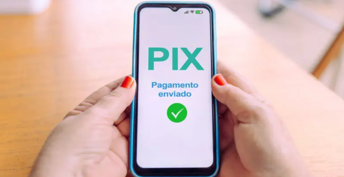 Imagem mostra celular na mão de uma pessoa com unhas pintadas de vermelho e no display aparece uma indicação de um pagamento via pix foi efetuado