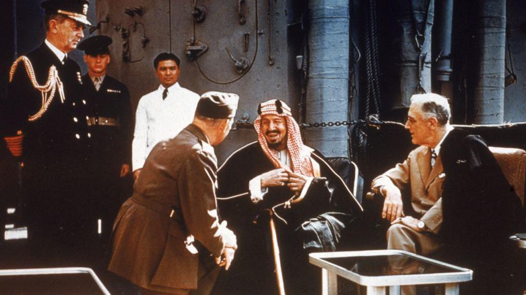O então presidente americano Franklin Delano Roosevelt reunido com o rei Ibn Saud, da Arábia Saudita, o chefe do Estado-Maior americano William D. Leahy (de joelhos) e o coronel William A. Eddy, a bordo do navio USS Quincy no canal de Suez, Egito, no dia 14 de fevereiro de 1945.