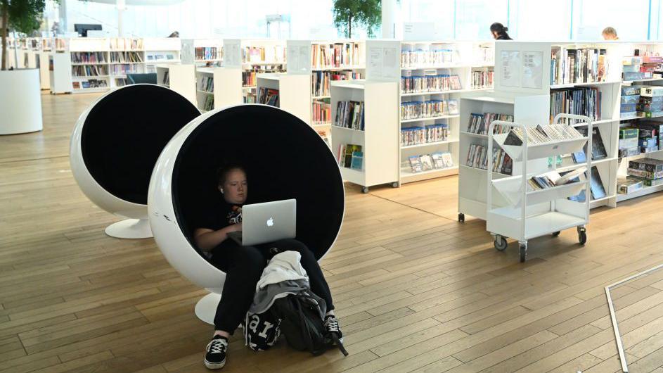 Una joven escribe en su computador portatil en la biblioteca