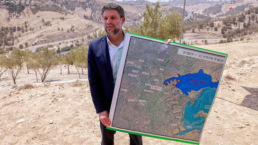 سموتريتش يقف في منطقة بالقرب من مستوطنة معالي أدوميم الإسرائيلية، ممسكاً بخريطة لما يعرف بمنطقة "إي 1"
