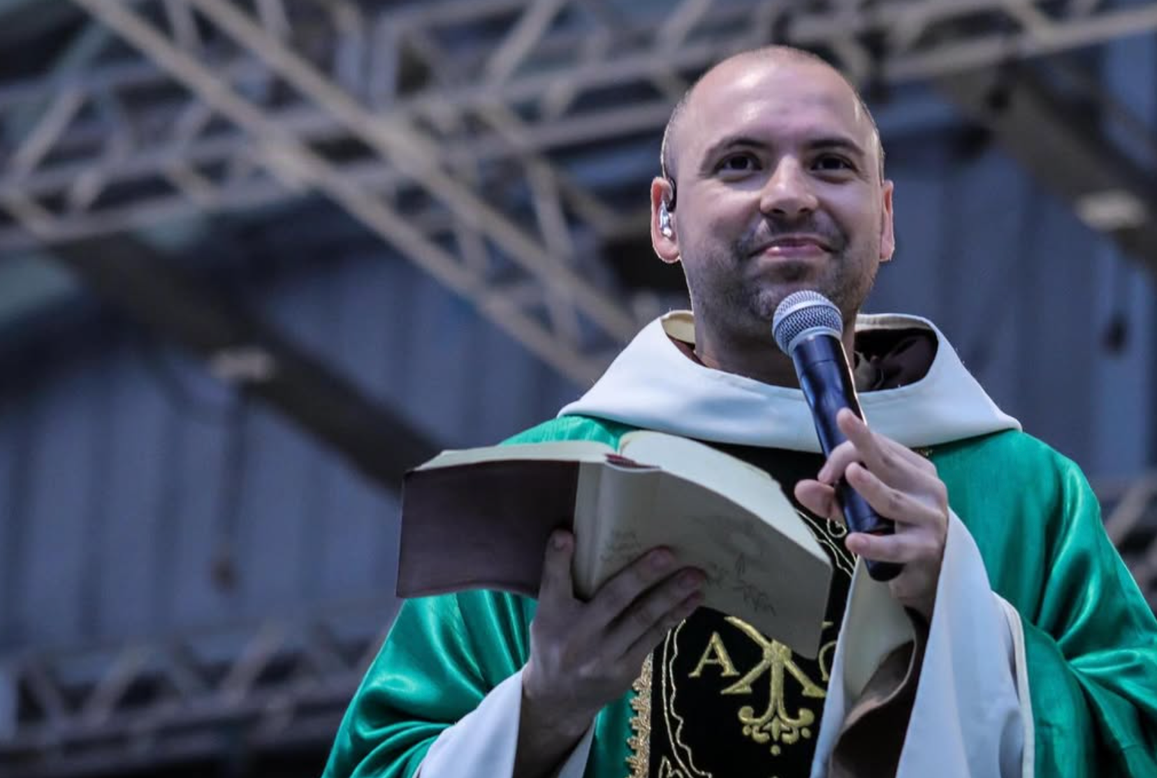 Frei Gilson usando indumentária religiosa e segurando a bíblia e um microfone com as mãos