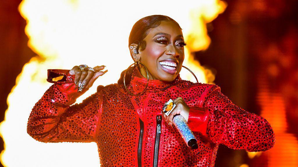 Missy Elliott con una cazadora de piel roja cantando mietras una ola de fuego se levanta tras ella.