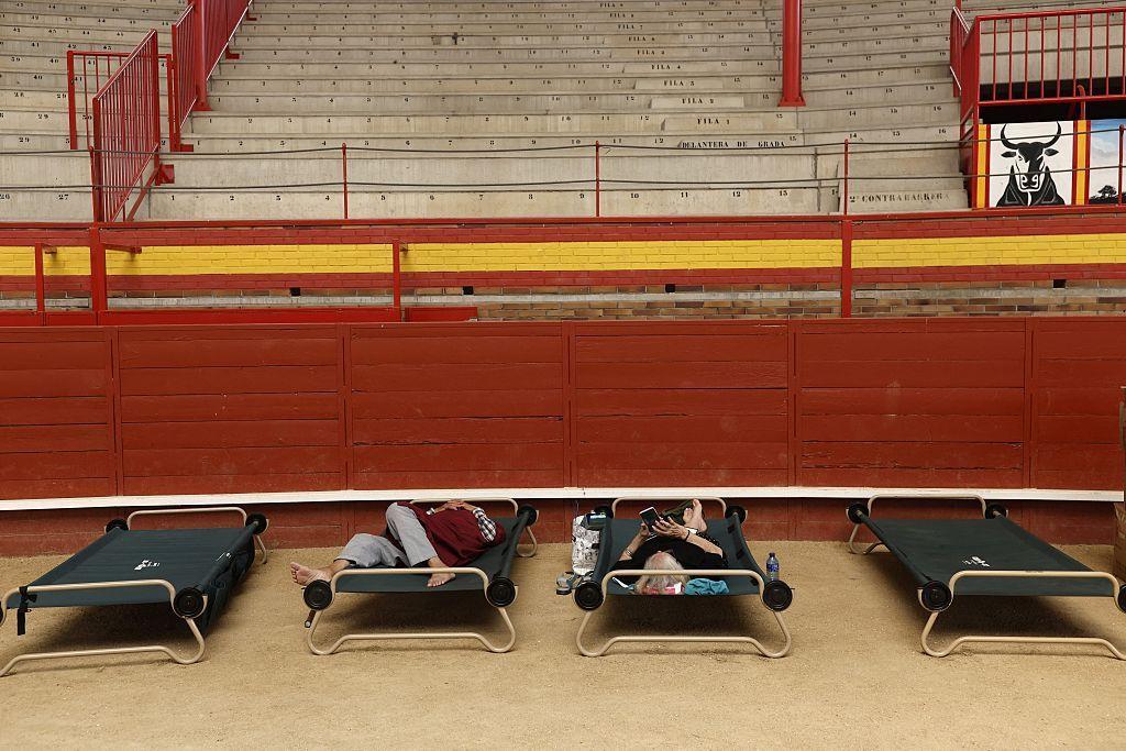 Cuatro camillas de campaña sobre el albero, la tierra de una plaza de toros. En dos de las camillas hay dos personas tumbadas. 