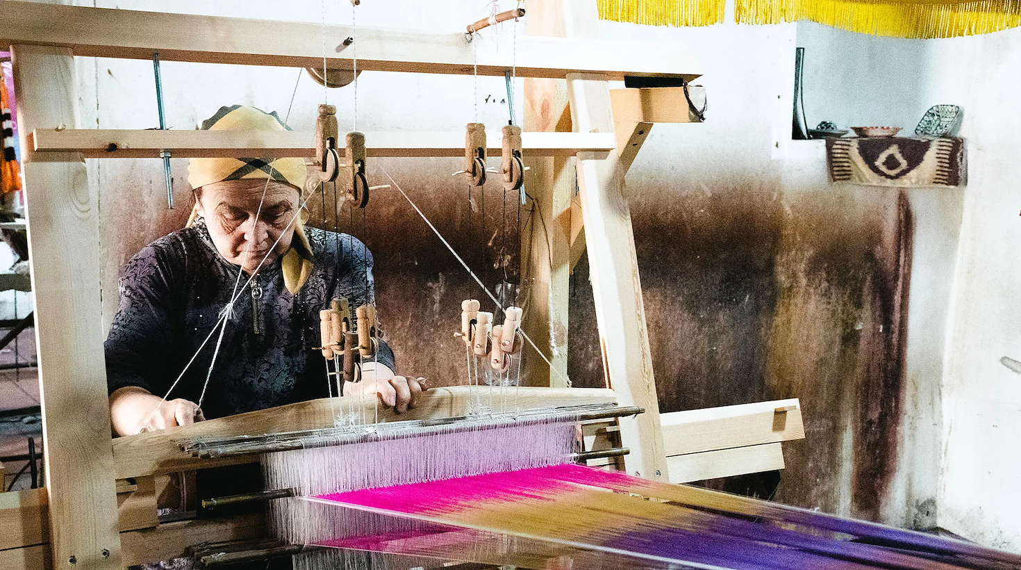 전통 베틀 앞에 앉은 여성이 실을 곱게 넘기며 천을 짜고 있다.