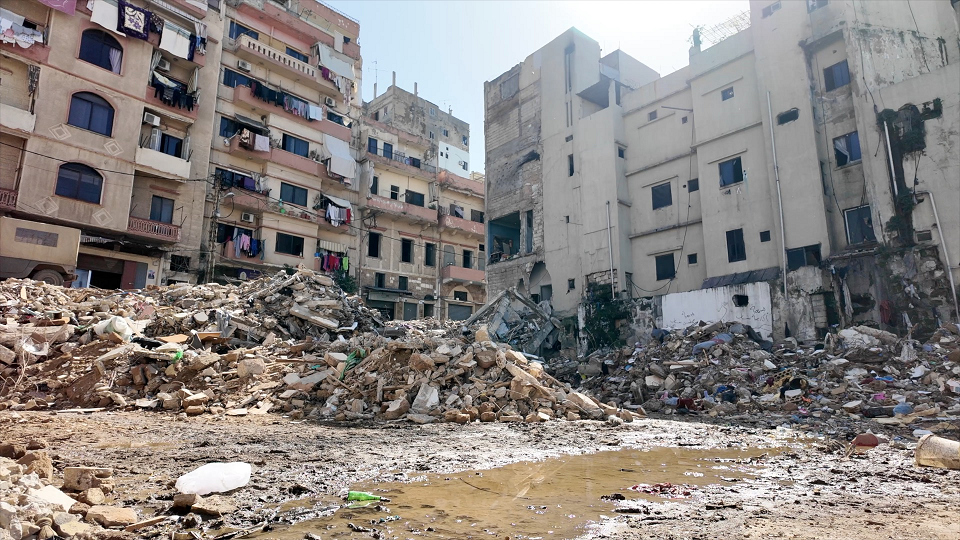 تُظهر الصورة بقايا أنقاض مبنى منهار، حيث تتناثر كتل الخرسانة والحديد بين الغبار في مشهدٍ يعكس حجم الدمار الذي خلّفه الانهيار.