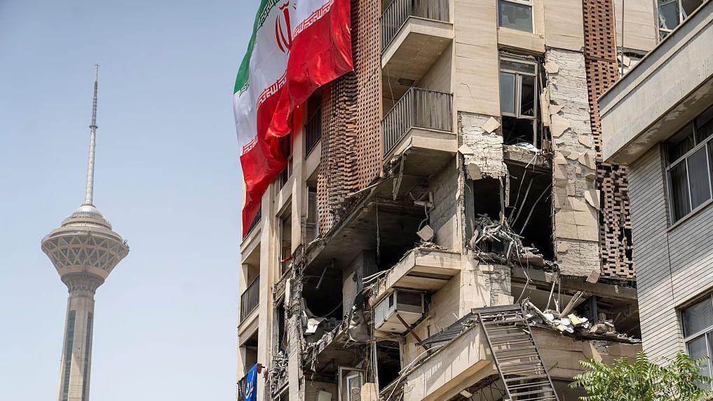 Una bandera iraní ondea en un edificio dañado durante los recientes ataques israelíes cerca de la Torre Milad en Teherán