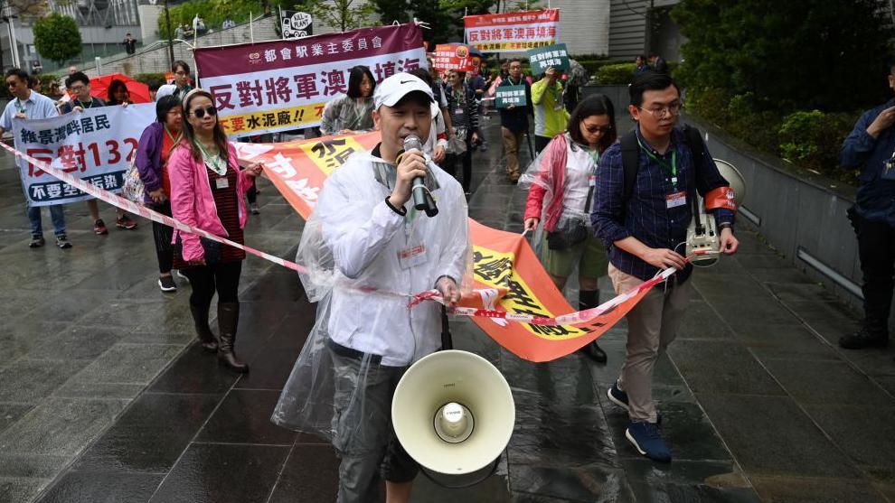 2023 年 3 月 26 日，一群居民反對將軍澳地區的填海計劃。參加者須戴掛頸卡牌，警方拉起封鎖線。