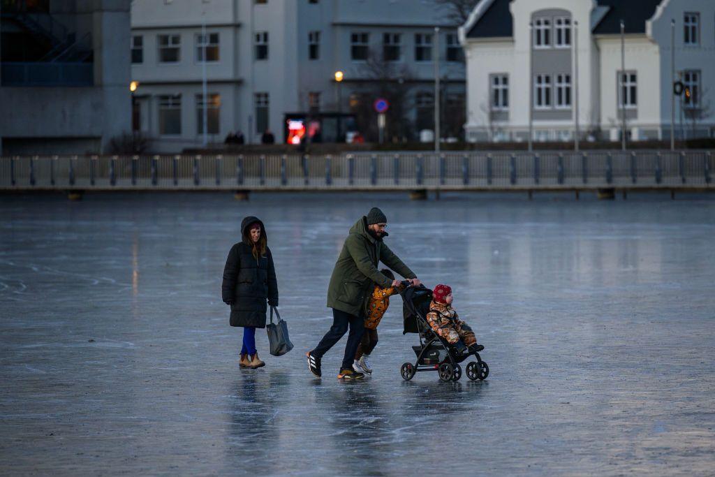 Família patinando no gelo, com casas em bom estado ao fundo