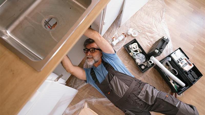 Muškarac popravlja cevi ispod sudopere