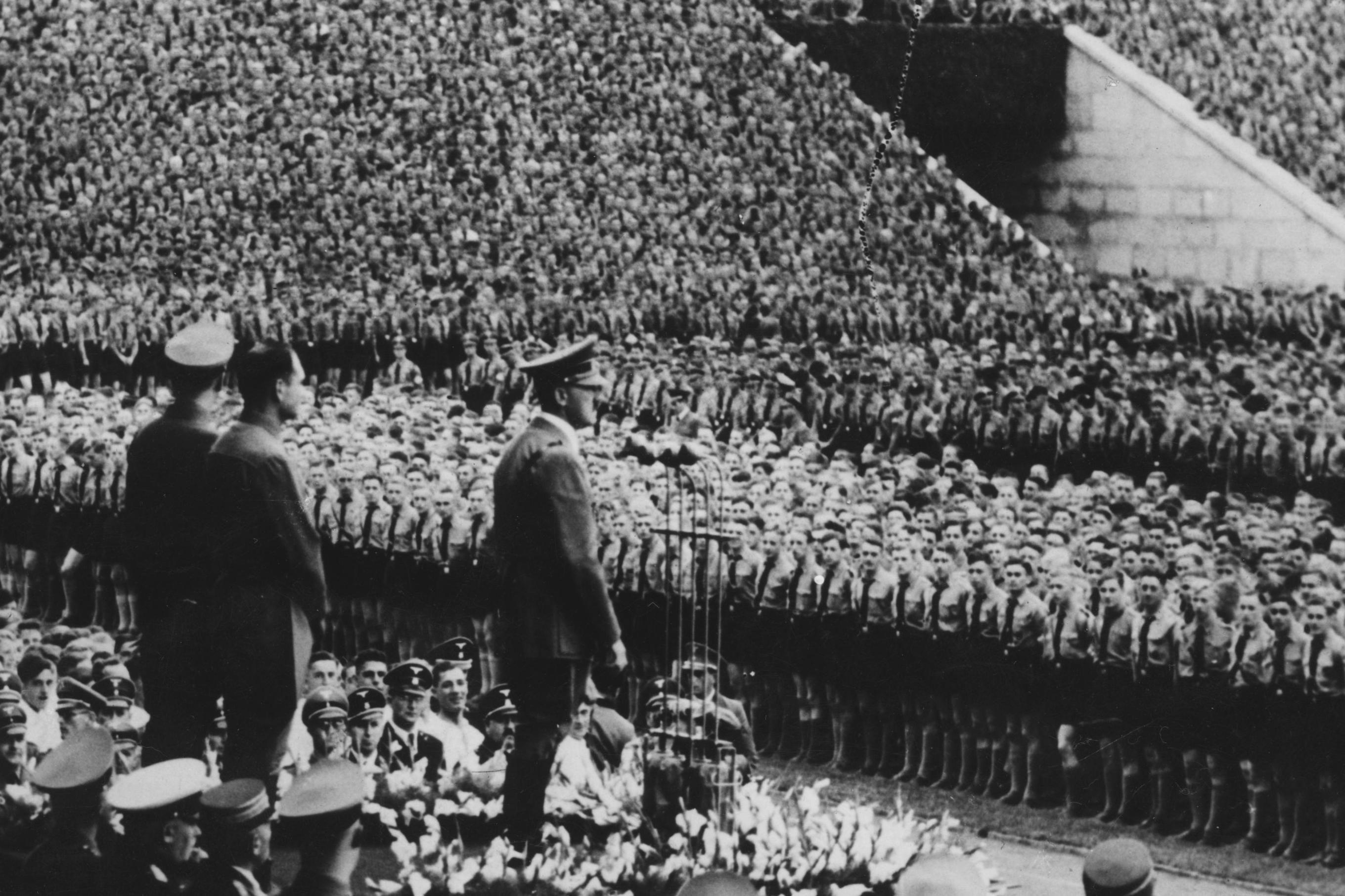 Adolf Hitler est&aacute; diante de milhares de jovens em um est&aacute;dio ao ar livre em 12 de setembro de 1938. Atr&aacute;s dele est&atilde;o Baldur von Schirach, l&iacute;der da Juventude Hitlerista, e Rudolf Hess, seu vice. 