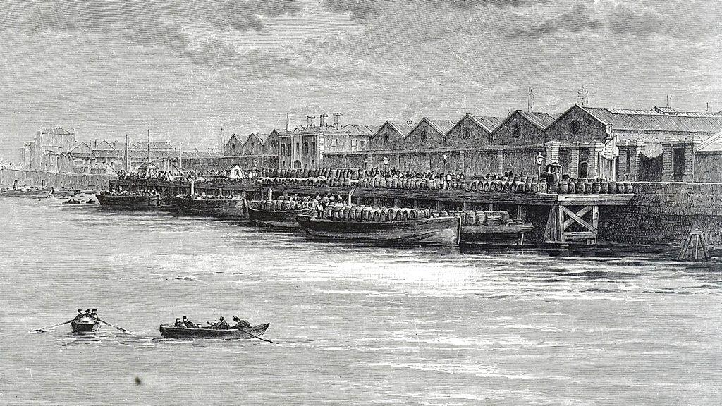 Un grabado antiguo muestra un puerto con almacenes y barcos cargados de barriles en la orilla, mientras pequeñas embarcaciones navegan en el río.