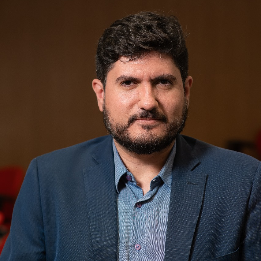 Guilherme Casar&otilde;es em retrato com semblante s&eacute;rio, camisa de bot&atilde;o e blazer azuis. 