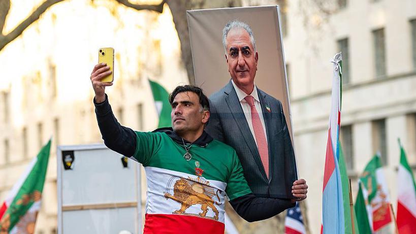 متظاهر يلتقط صورة سيلفي وهو يحمل صورة محمد رضا بهلوي خلال مظاهرة في لندن مناوئة للسلطات الإيرانية في 3 يناير/كانون الثاني 2026