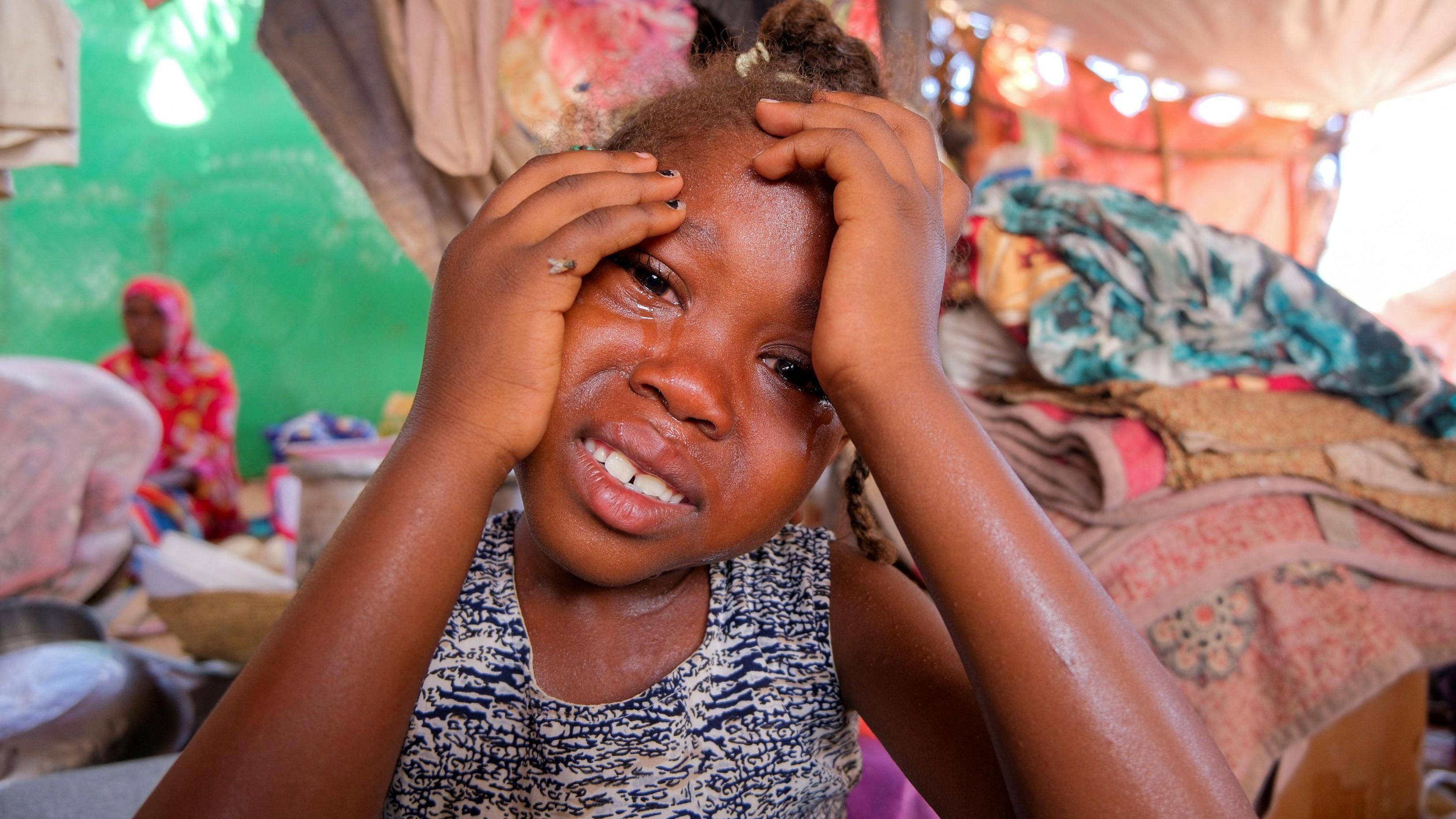Foto de uma criança sudanesa chorando com as mãos no rosto. 