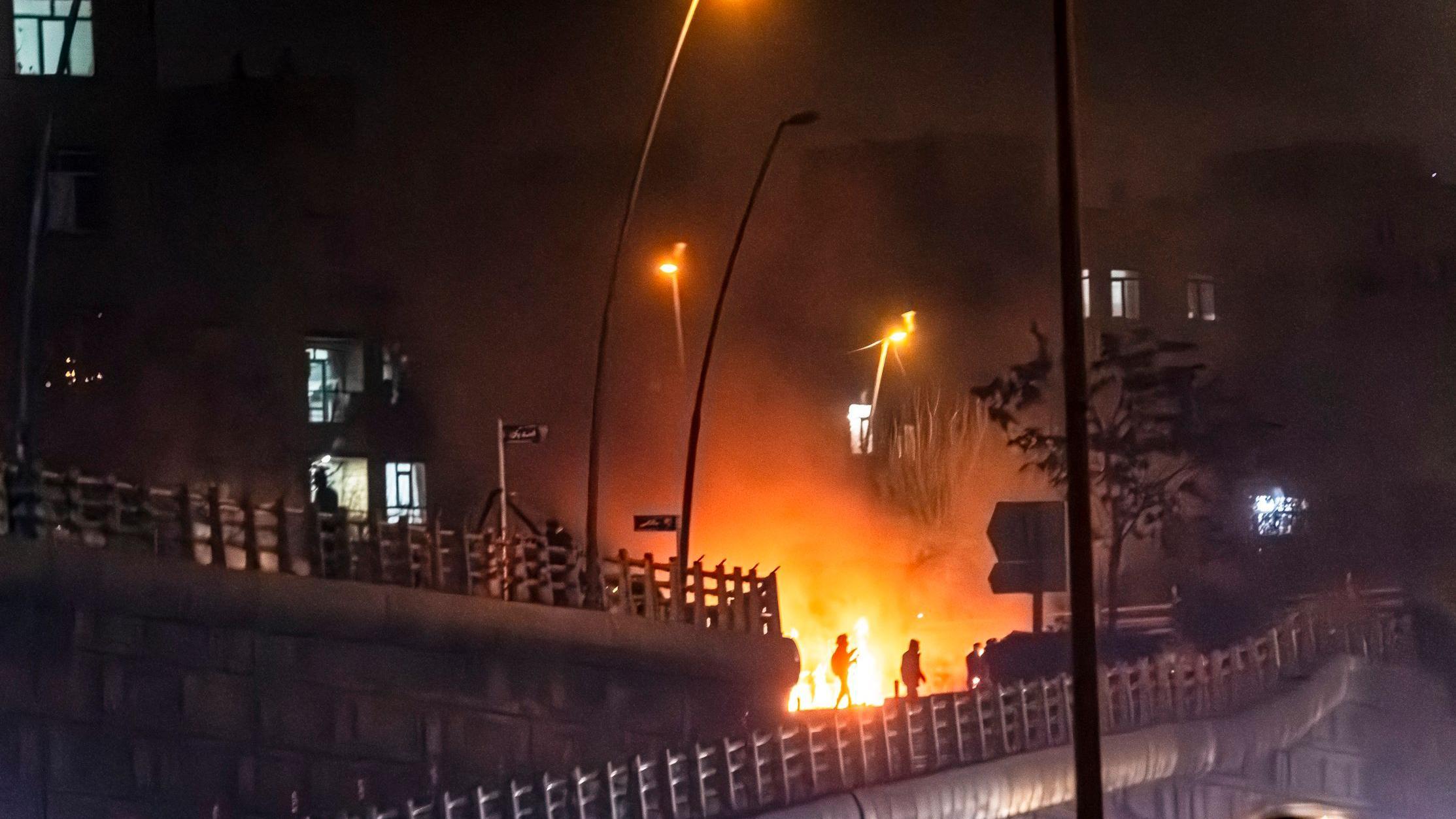 يظهر عنصر مسلح من قوات الأمن الإيرانية أمام مبنى محترق خلال احتجاجات في طهران، إيران، في 9 يناير/كانون الثاني 2026. 