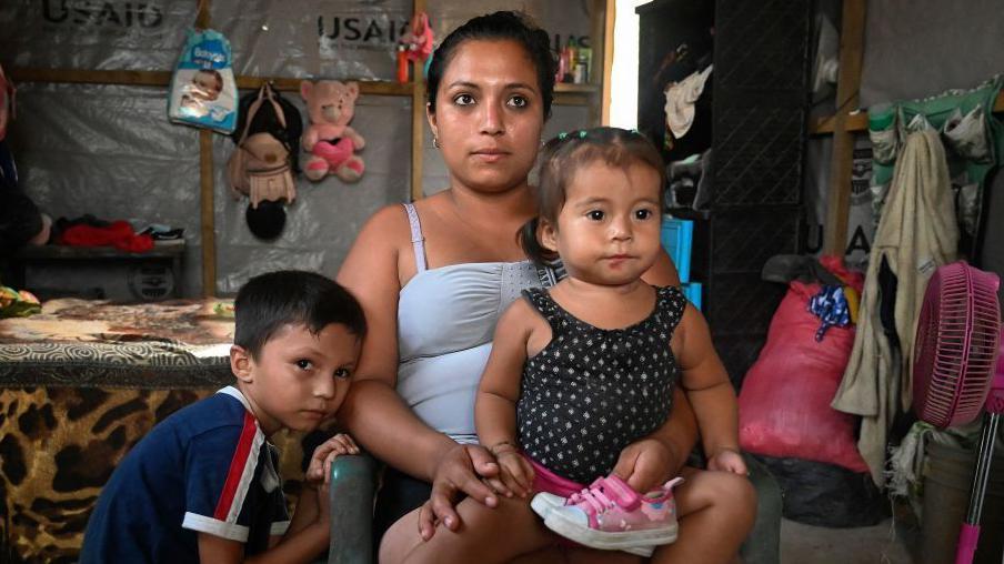 Sandra Ramos y sus hijos en una choza improvisada que construyó con ayuda de  (USAID) después de un huracán (julio de 2022).