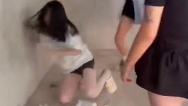 一張模糊的截圖顯示，一名身穿白色T恤和短褲的女孩倒在地上，周圍站著兩名身穿黑色衣服的女孩。