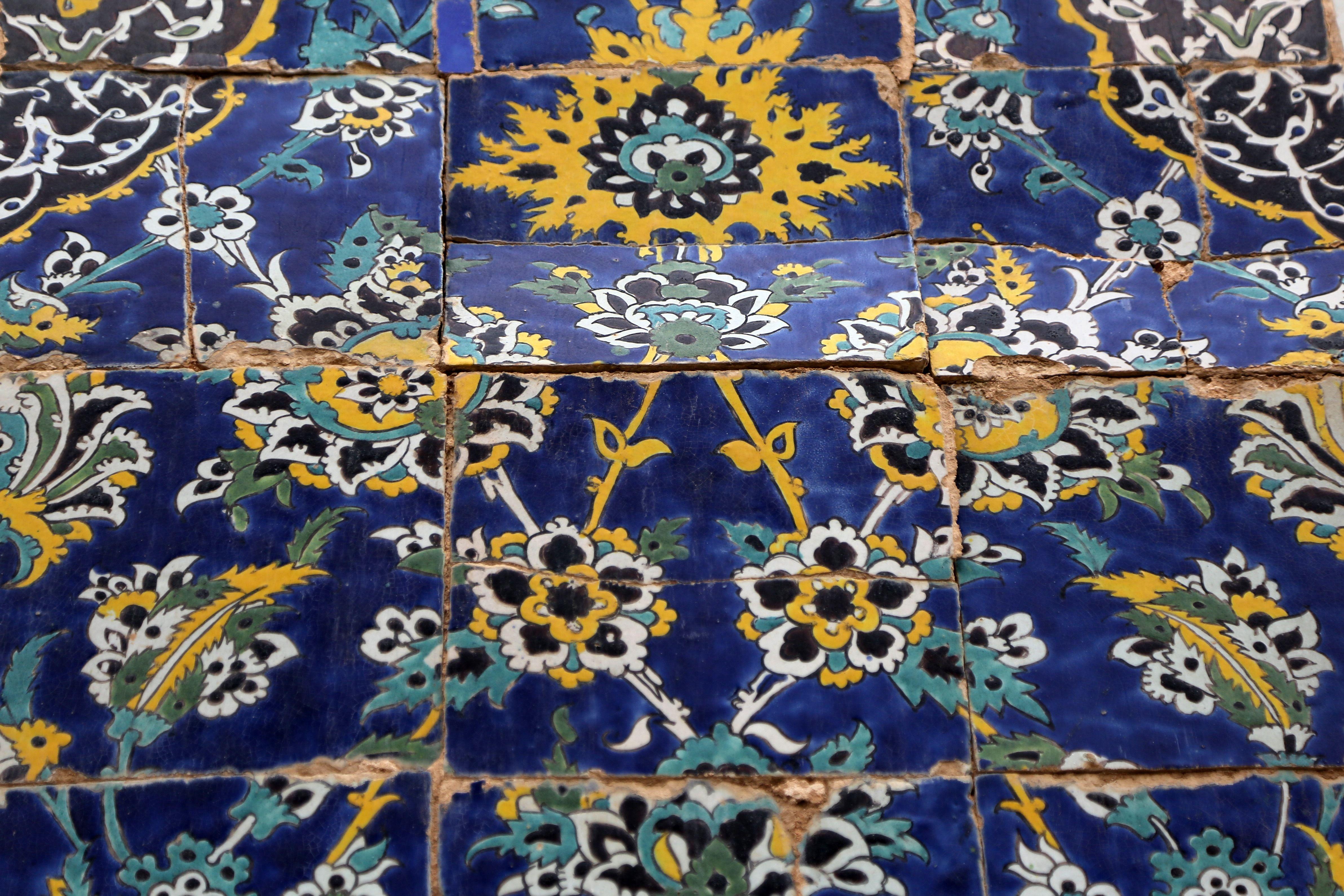 Los azulejos islámicos, con intrincados patrones, se agrietan bajo tensión. Presentan motivos florales en azul, amarillo, negro y blanco.