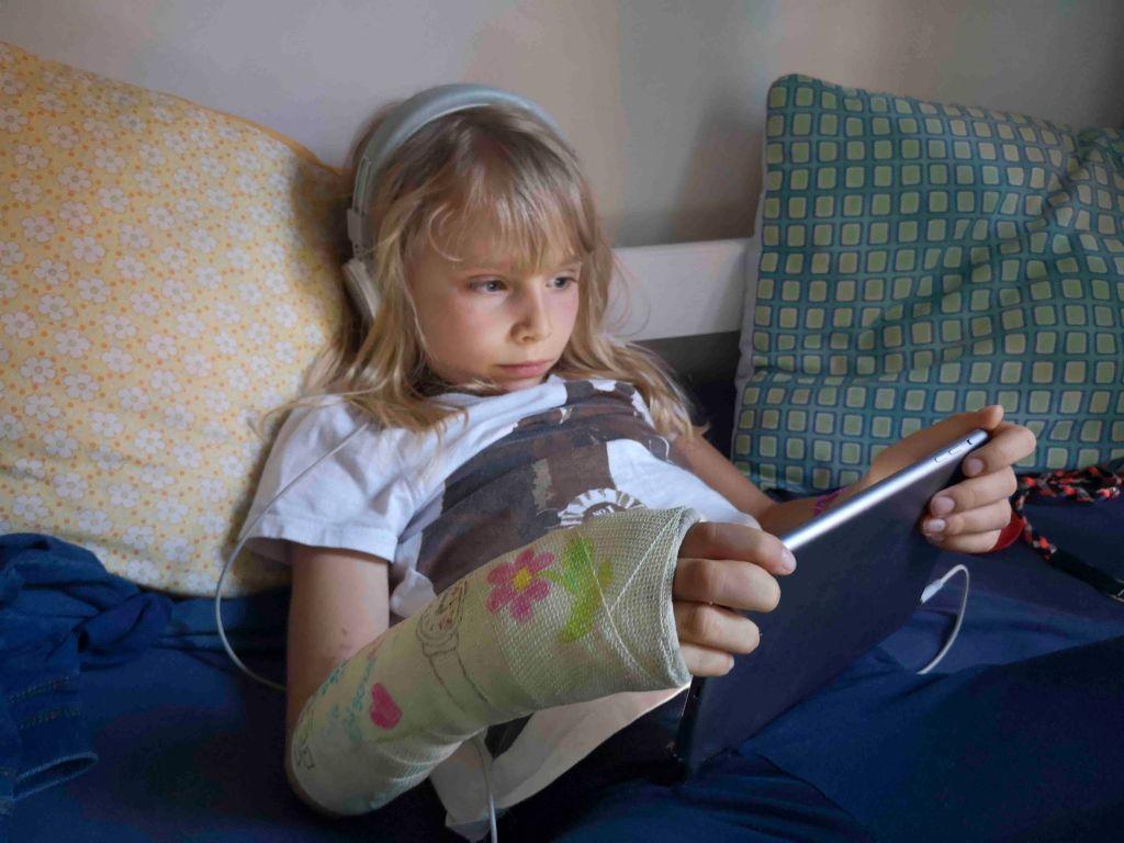 Uma criança sentada na cama com fones de ouvido e um iPad na mão