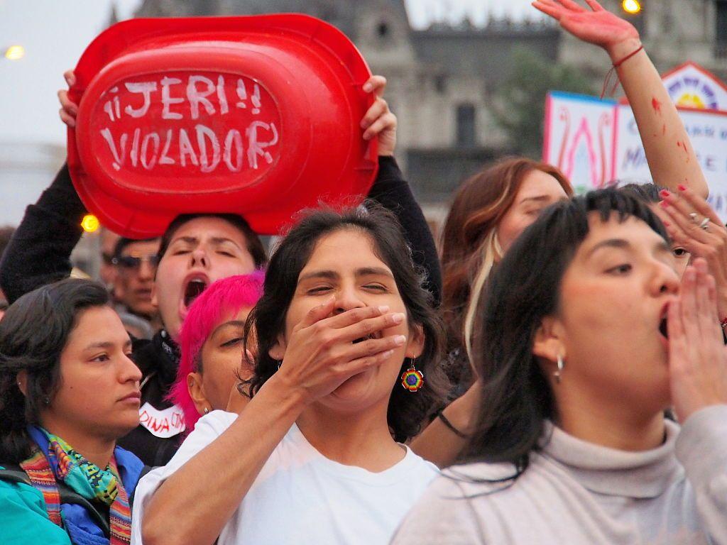 "Jeri violador" puede leerse en el fondo de una pequeña bañera de color rojo. La sostiene una mujer que tiene la boca abierta, gritando. Hay a su alrededor más mujeres que protestan.