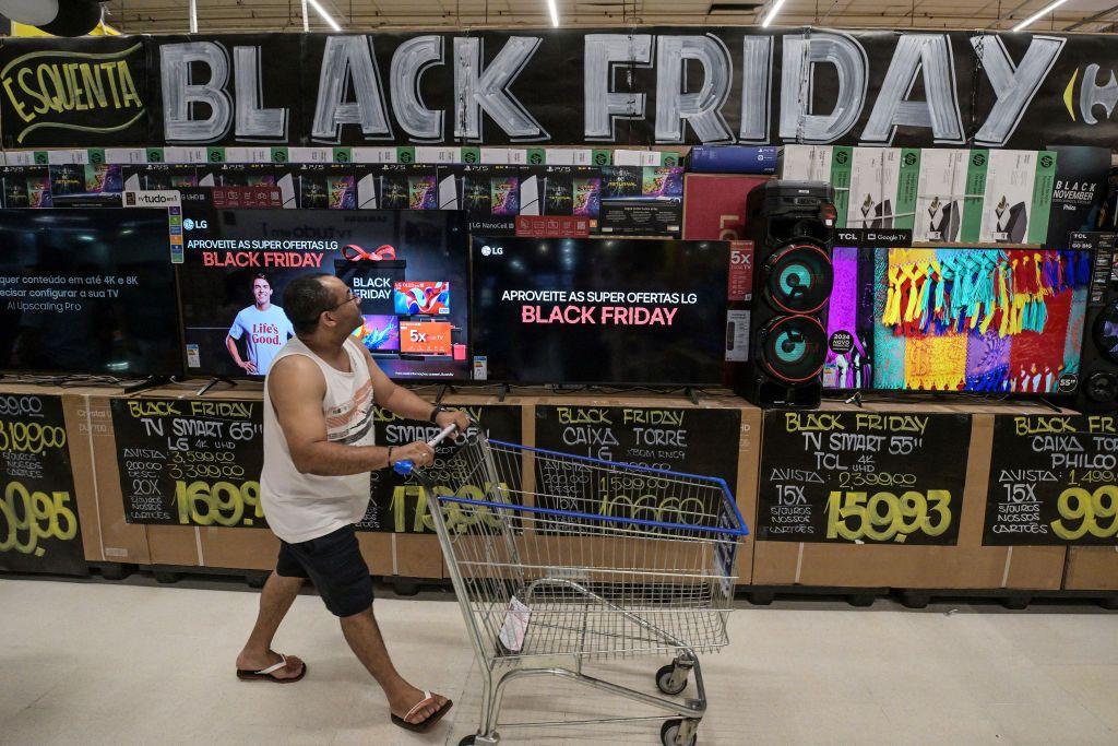 Homem anda com carrinho de compras em uma loja cheia de placas de promoção da Black Friday