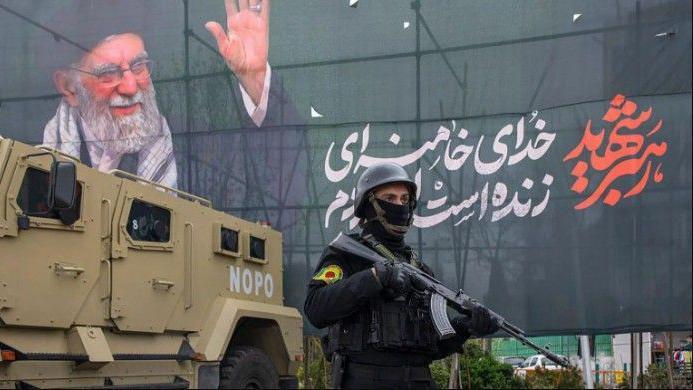 صورة لجندي إيراني أمام مصفحة ومن روائهما لوحة إعلانية كبيرة تحمل صورة المرشد السابق علي خامنئي 