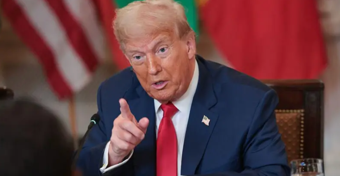 Donald Trump usando terno azul marinho e gravata vermelha e apontando o dedo indicador enquanto fala
