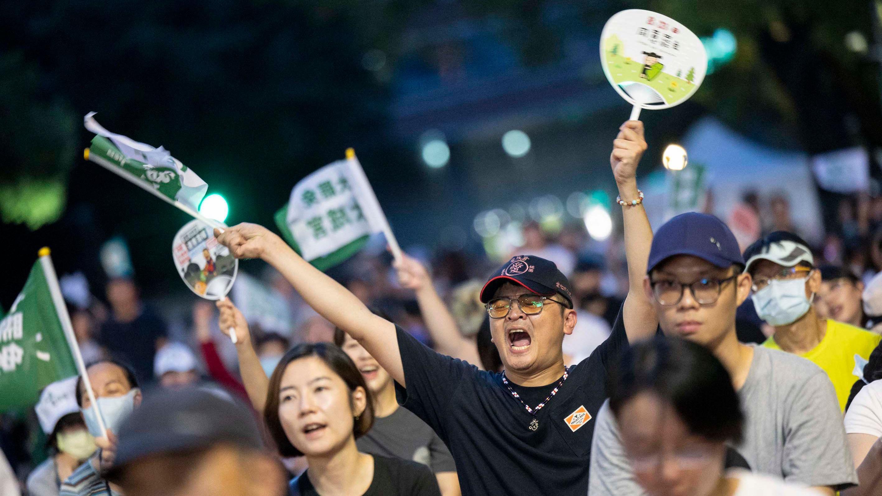台灣民眾參與大罷免選後集會，一位身穿黑色汗衫，戴上鴨舌帽男士喊著口號舉起小旗幟與紙扇（26/7/2025）