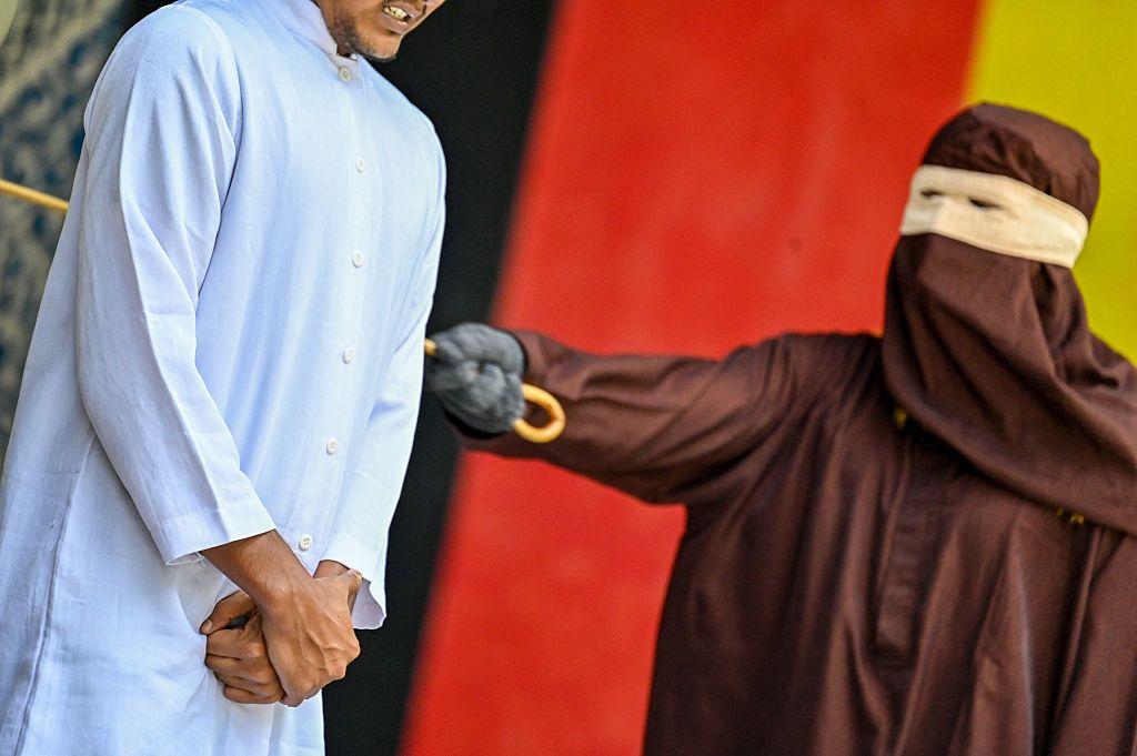 يبدي رجل رد فعل أثناء تنفيذ شرطة الشريعة عقوبة الجلد علنًا عليه في إقليم آتشيه بإندونيسيا، يوم 7 أبريل/نيسان 2026، بعد إدانته بممارسة الجنس خارج إطار الزواج. ويظهر الرجل مرتدياً جلباباً أبيض، فيما لا تبدو ملامح رأسه في الصورة، بينما يقف شخص مغطى الوجه والرأس وهو يجلده بسوط. ويُعد آتشيه الإقليم الوحيد في إندونيسيا الذي يطبق أحكام الشريعة الإسلامية على المستوى المحلي.