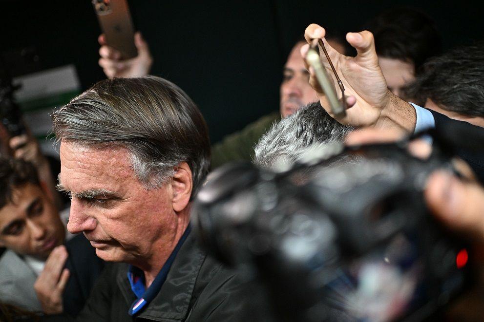 Bolsonaro olhando para a frente com olhar sério, rodeado por jornalistas