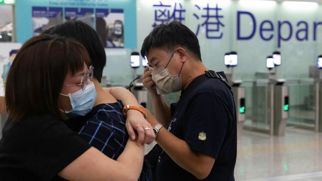 在香港機場的離港閘前，兩人相擁，另外一人以紙巾抹眼淚。